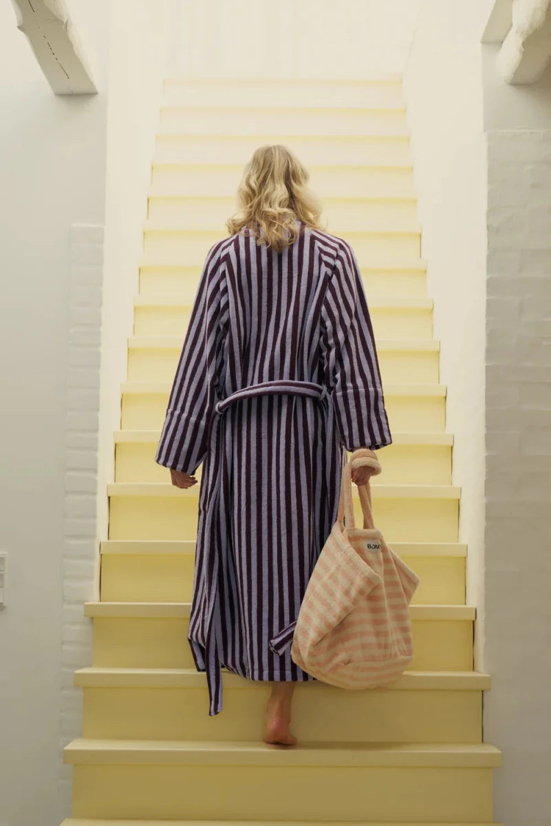 Bongusta Naram Bathrobe in wine and lavender blue, soft fabric, displayed on a bathroom hook with a weekend bag in the background