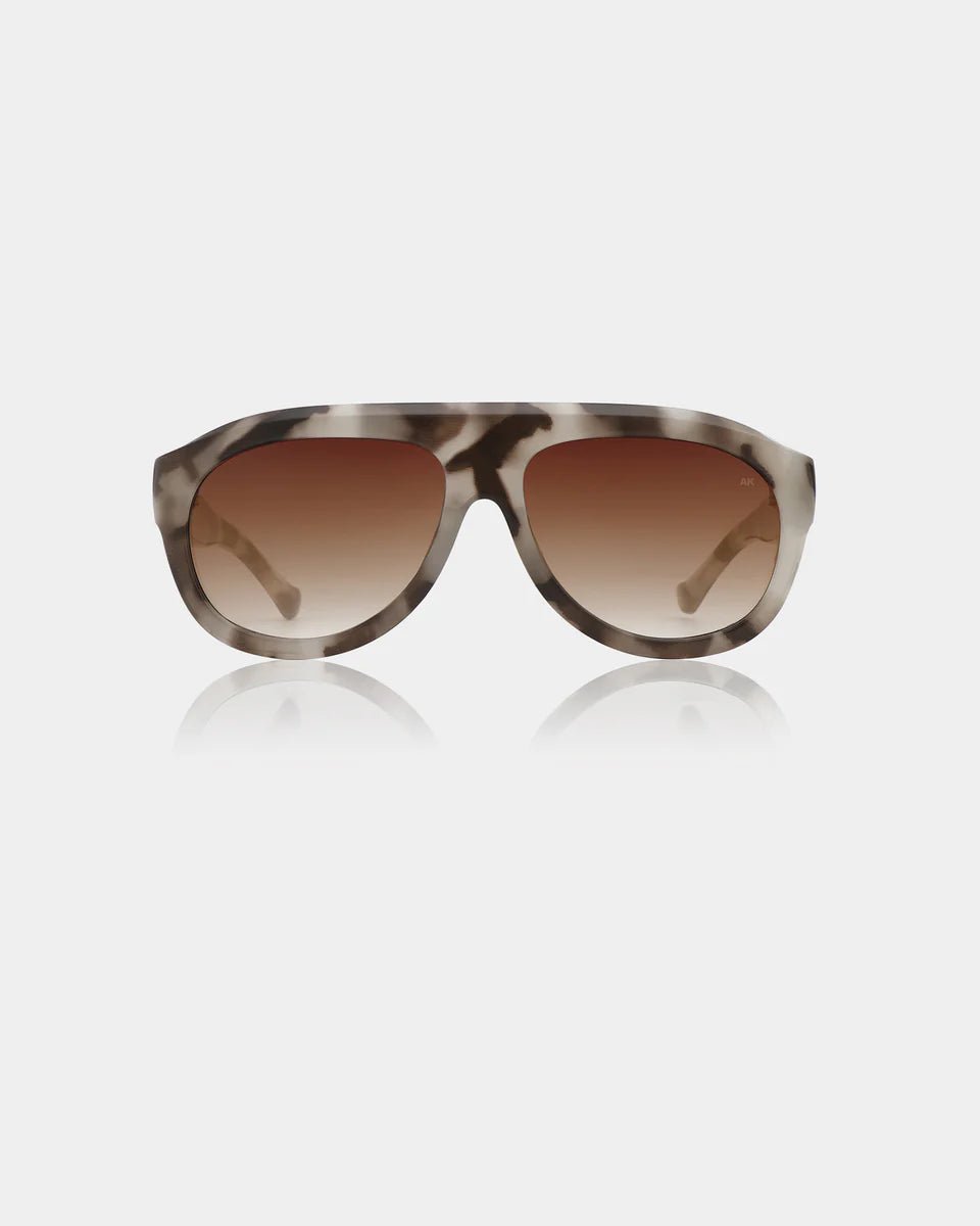 A. Kjaerbede Rio sunglasses with cookie dough-colored frames and dark tinted lenses on a white background.