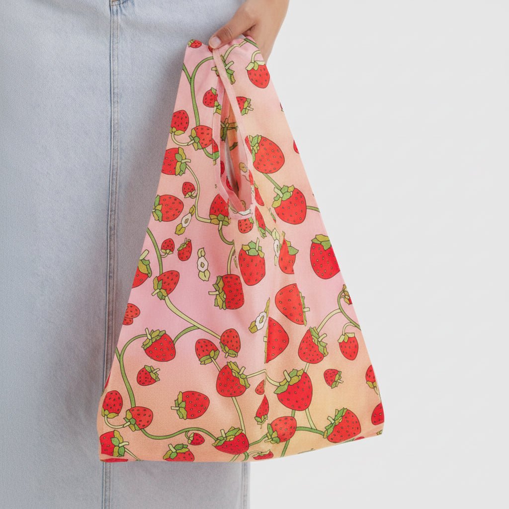 Reusable bag with strawberry pattern held by a person against a gray background