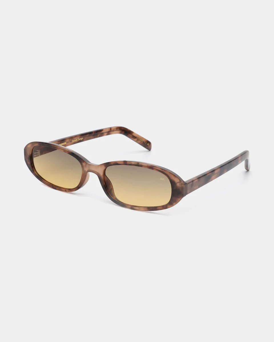 A. Kjaerbede Macy sunglasses with large rounded frames and tinted lenses, stylishly worn on a person outdoors.