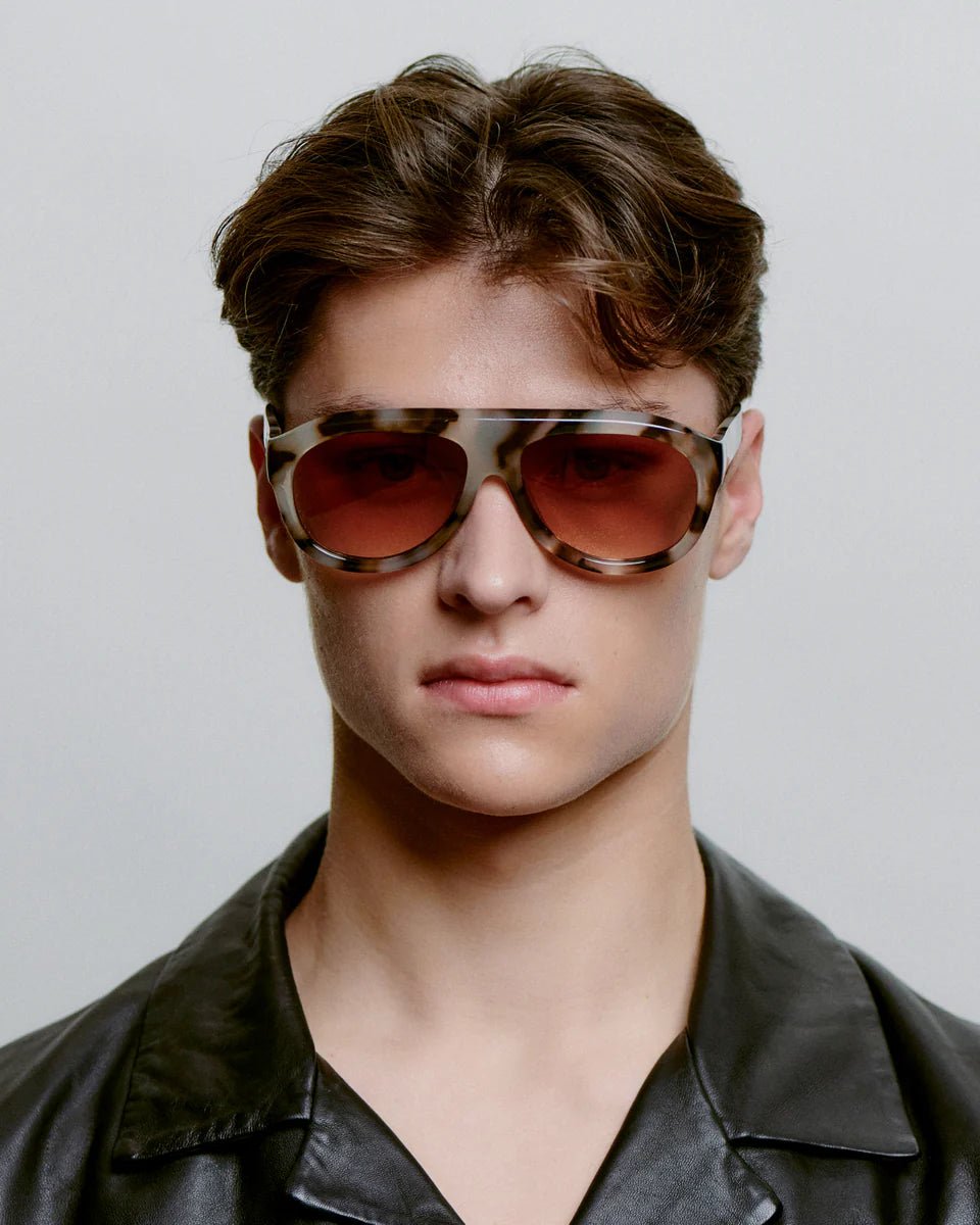 A. Kjaerbede Rio sunglasses with rounded frames and tinted lenses, stylishly worn by a person outdoors.
