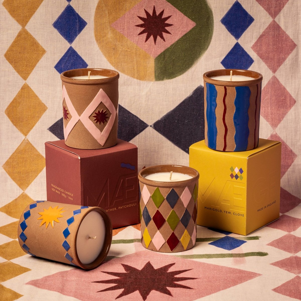 Decorative candles with geometric patterns on a colorful geometric-patterned fabric background.