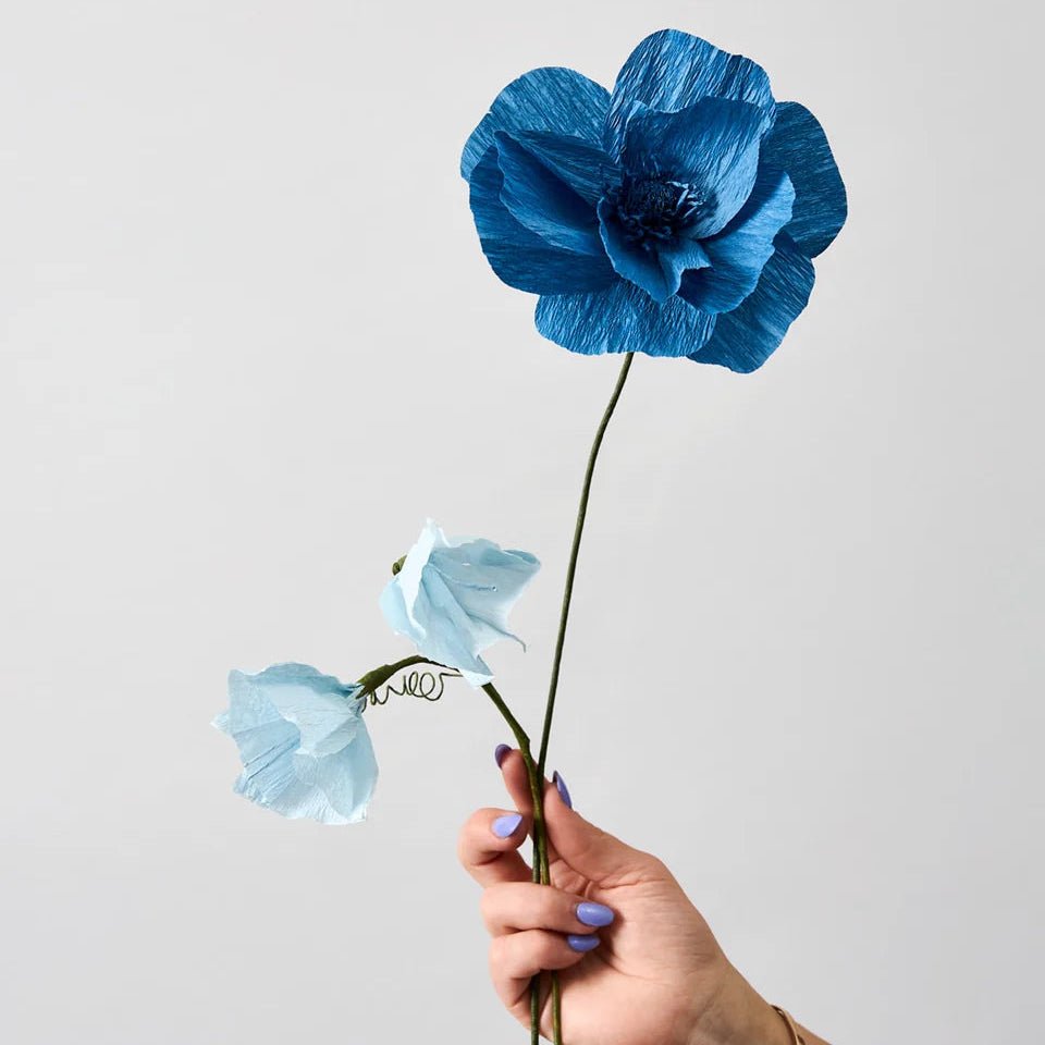 Hand holding a blue paper flowers against a light gray background