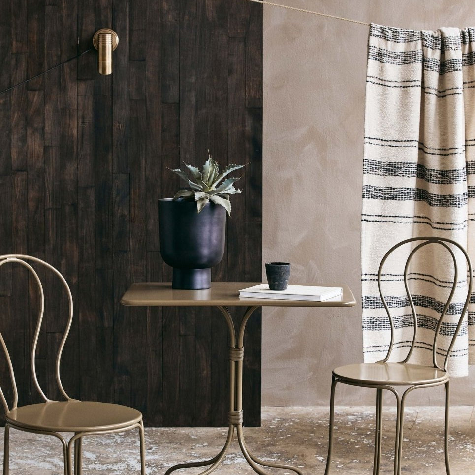 Two metal chairs and a small table against a textured wall with a plant and decorative item.