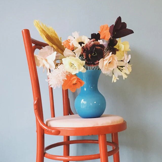 Blue vase with flowers on a red chair against a light blue wall