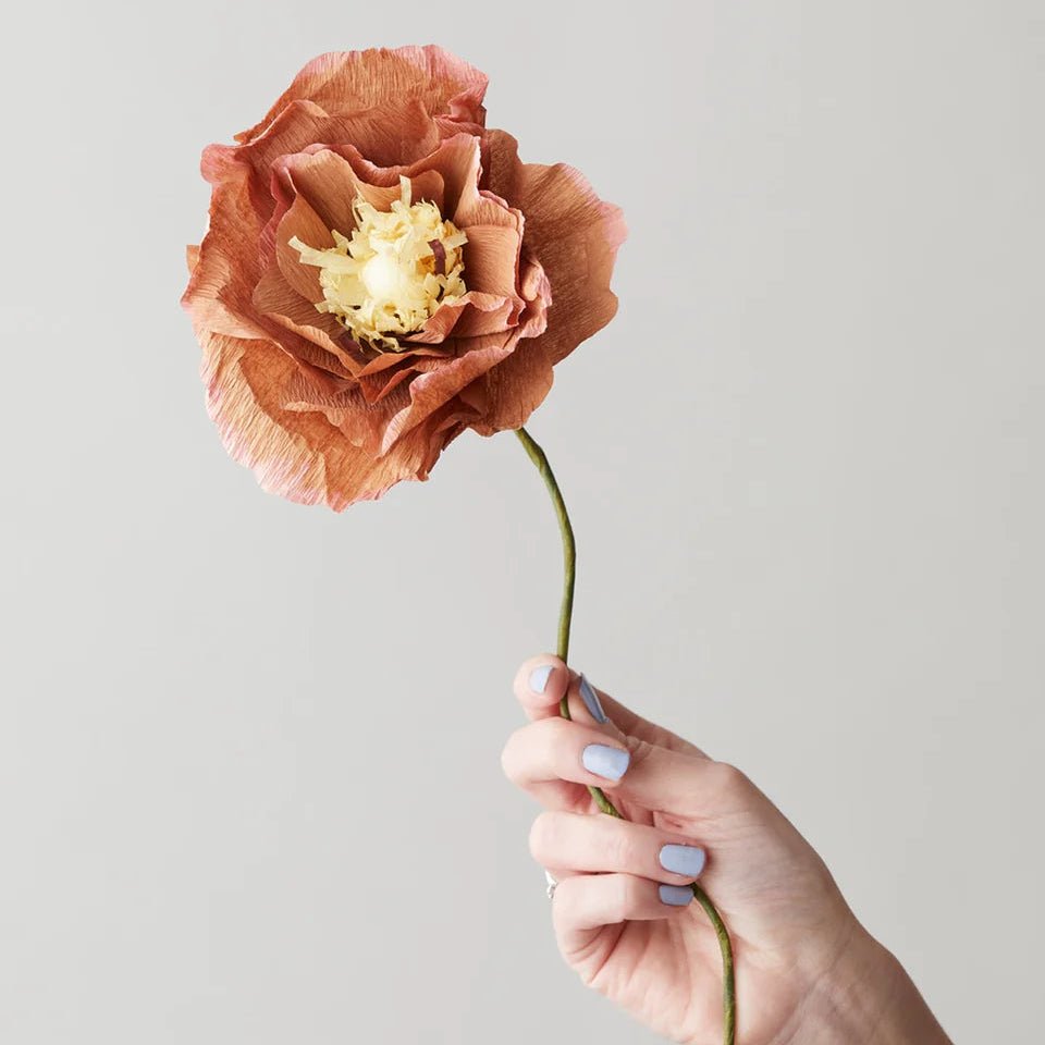 Hand holding a large artificial flower against a plain background