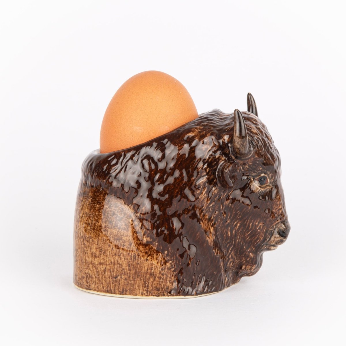 Ceramic buffalo-shaped egg holder with an egg on a white background