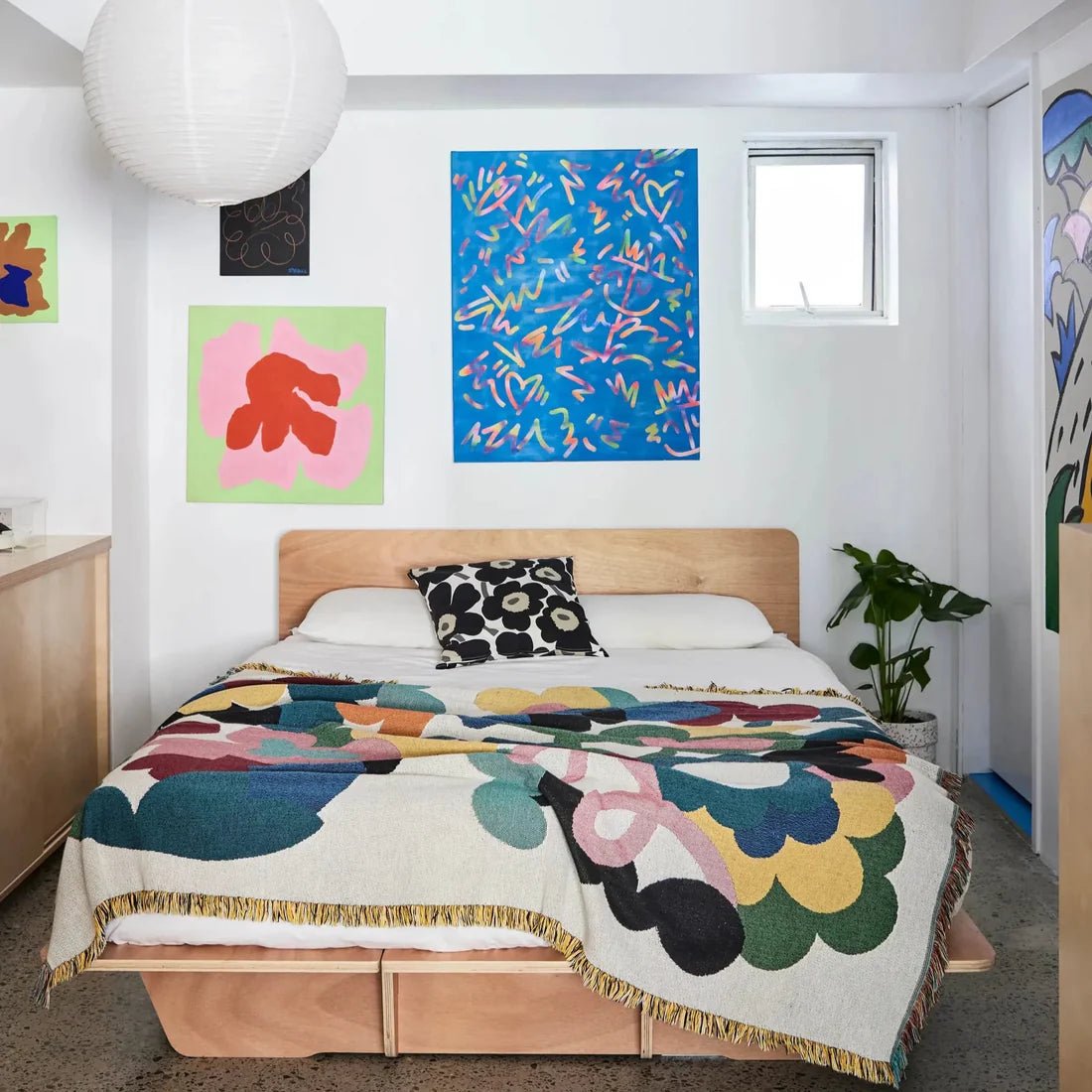 Bedroom with colorful floral blanket, abstract art on the wall, and a plant.