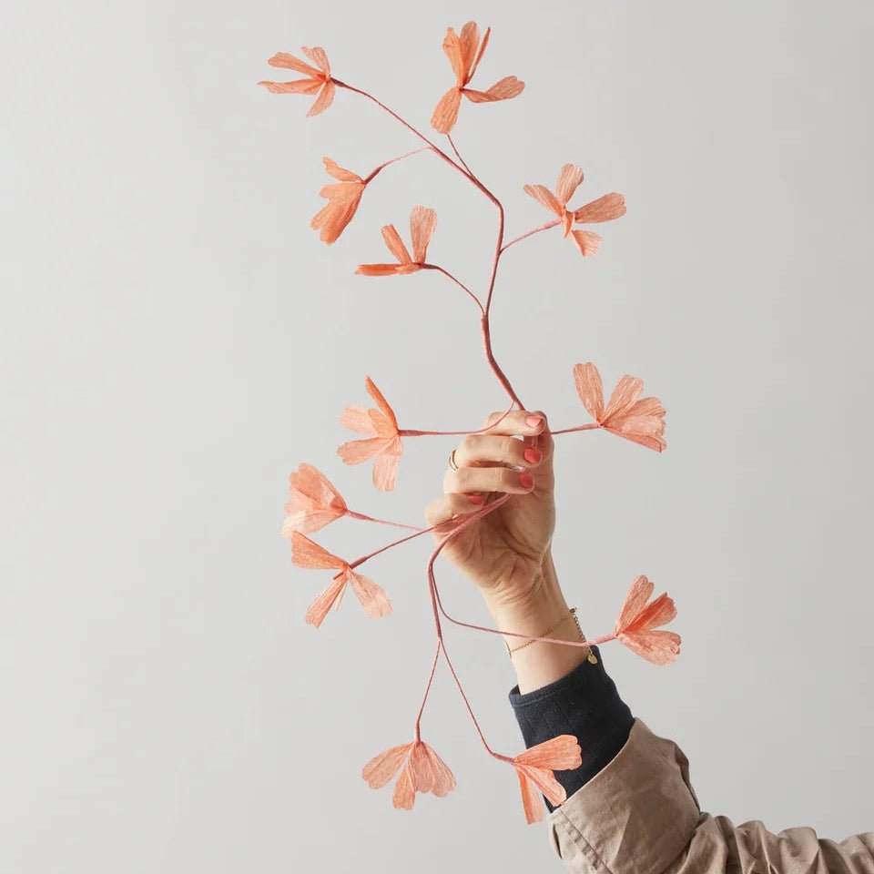Person holding a branch with pink flowers against a light gray background