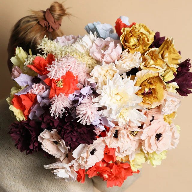 Person holding a large bouquet of colorful flowers against a beige background