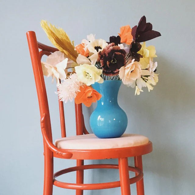 Blue vase with flowers on a red chair against a light blue wall