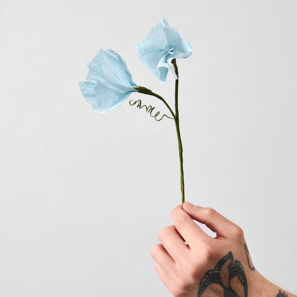 Hand holding two blue paper flowers against a light gray background