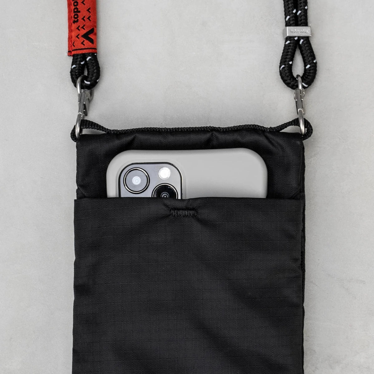 Black crossbody bag with a phone inside on a light gray background