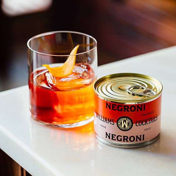 Williams Premium Canned Cocktails Negroni cocktail in a clear can with vibrant orange and red hues, garnished with an orange slice.