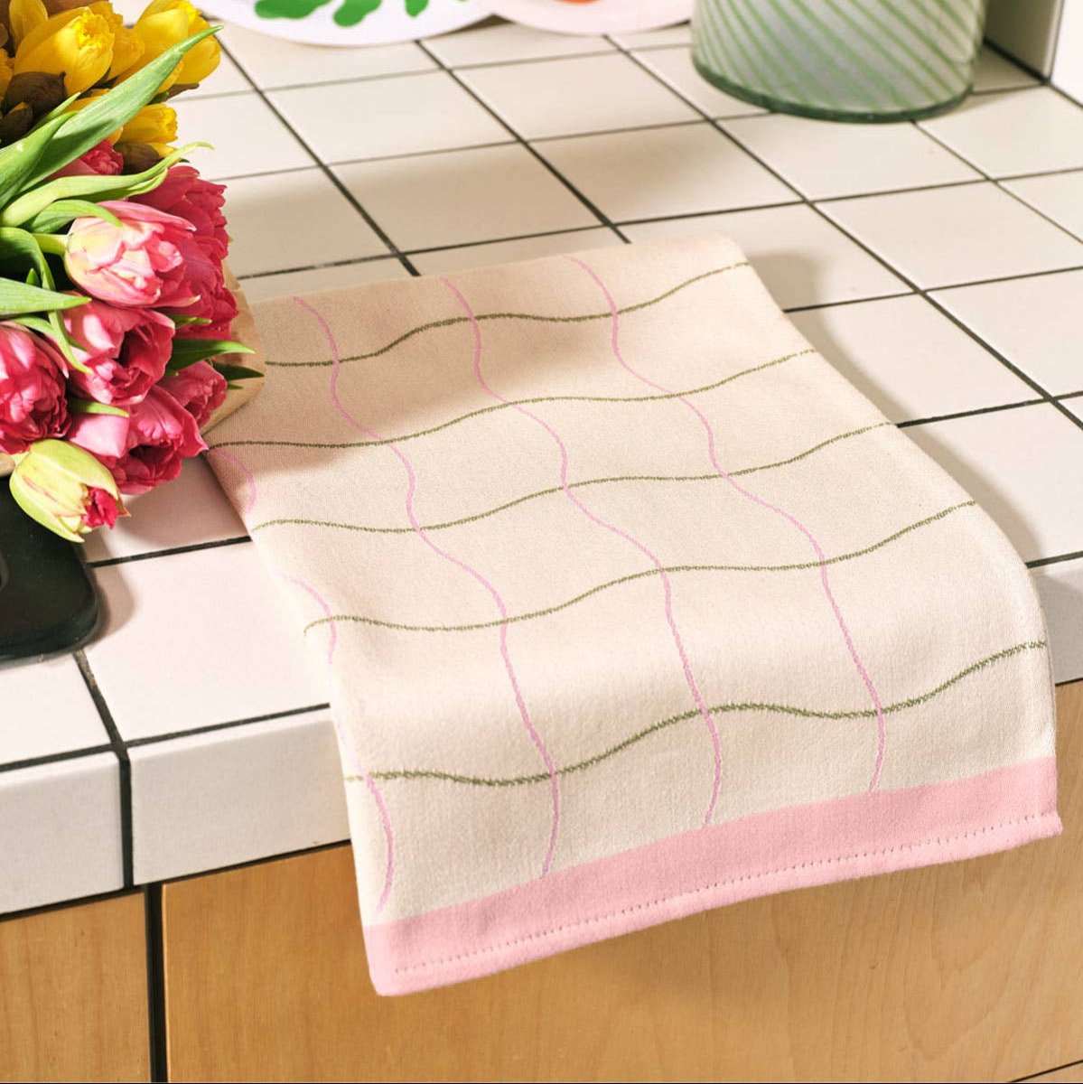 Beige towel with pink border on a tiled surface with flowers in the background