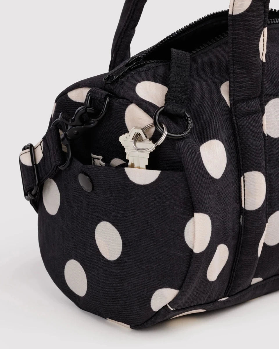 Black and cream polka dot nylon duffle bag by Baggu, showing a spacious design with sturdy handles and a compact shape.