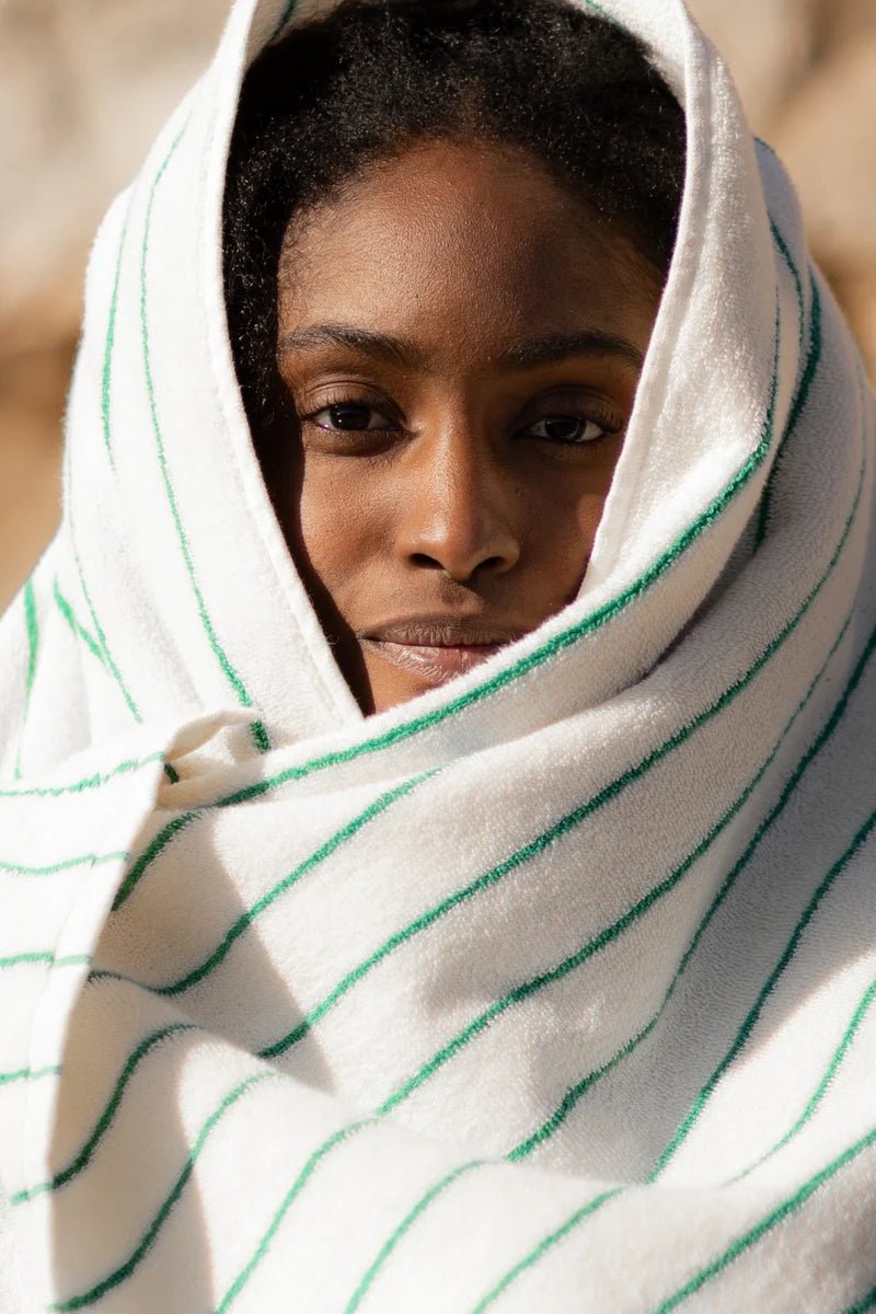 Soft white and grass green Naram bathroom towel by Bongusta displayed outdoors in a desert setting.
