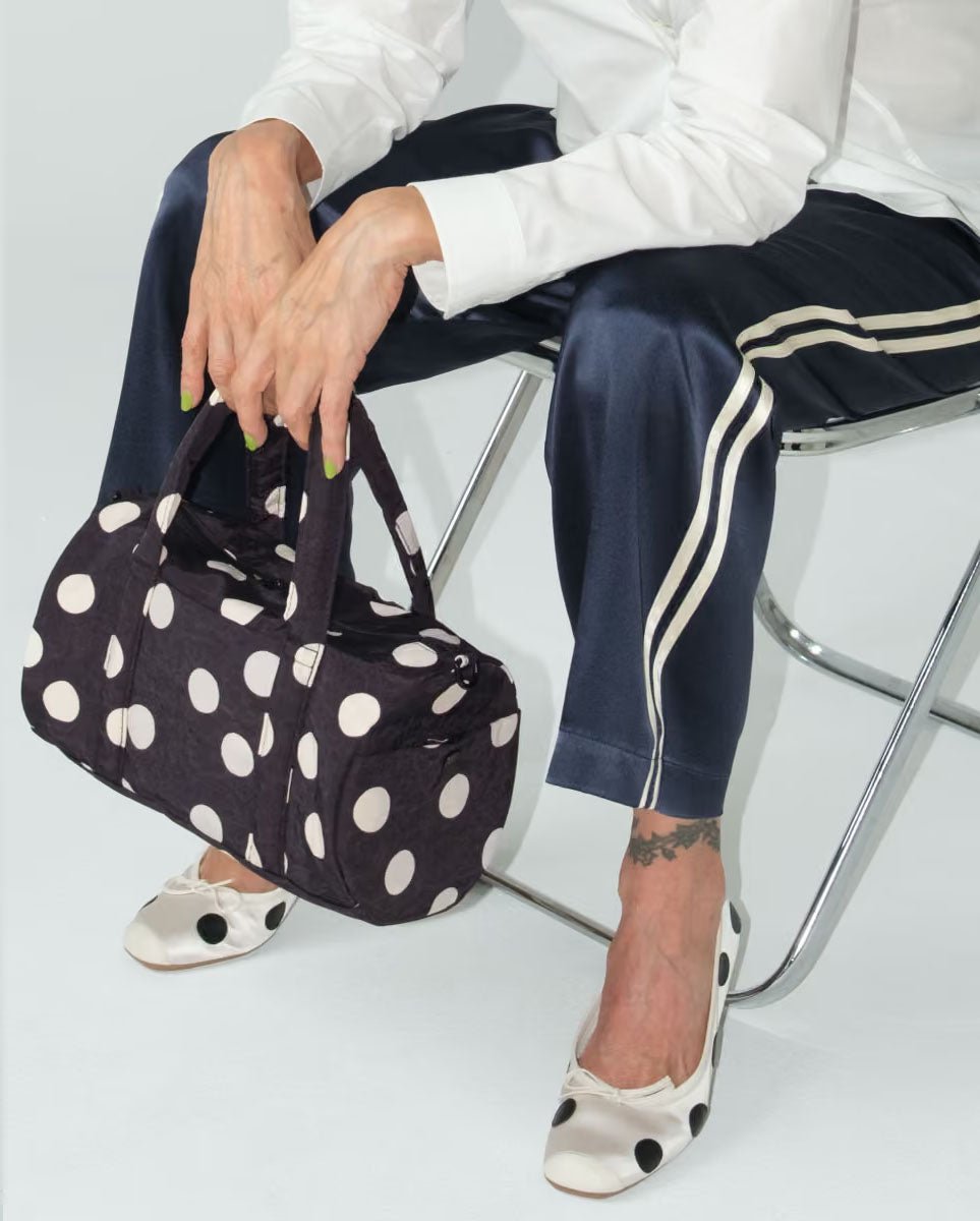 Black and cream polka dot nylon duffle bag by Baggu, featuring a spacious, lightweight design with sturdy handles and a zipper closure.