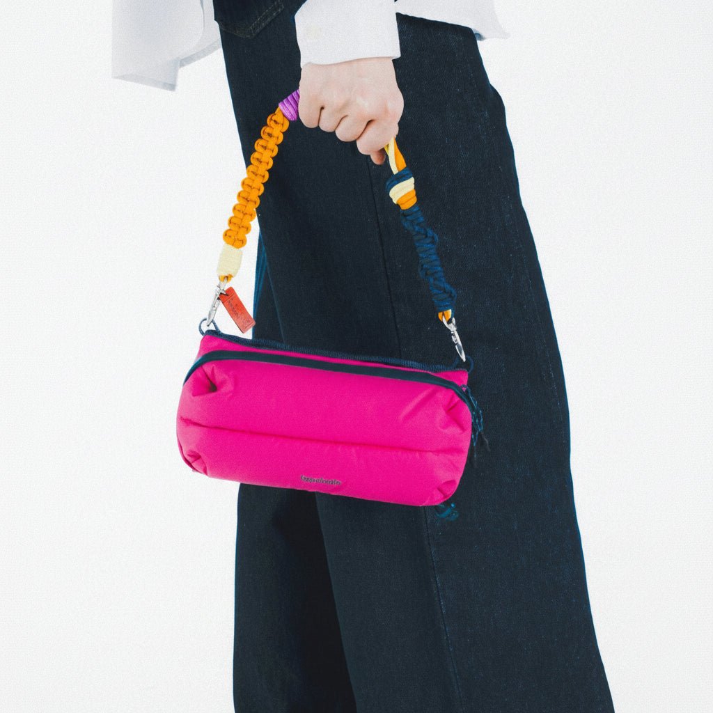 Person holding a pink puffy topologie 
bag with colorful handle against a white background