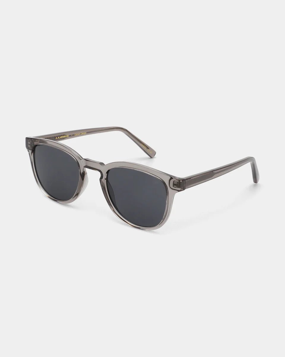 Grey-transparent Bate sunglasses by A. Kjaerbede with angular frame, shown from a side angle.
