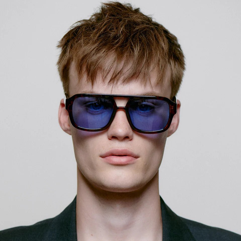 A. Kjaerbede Kaya sunglasses with round frames and dark tinted lenses, stylishly worn on a model outside.