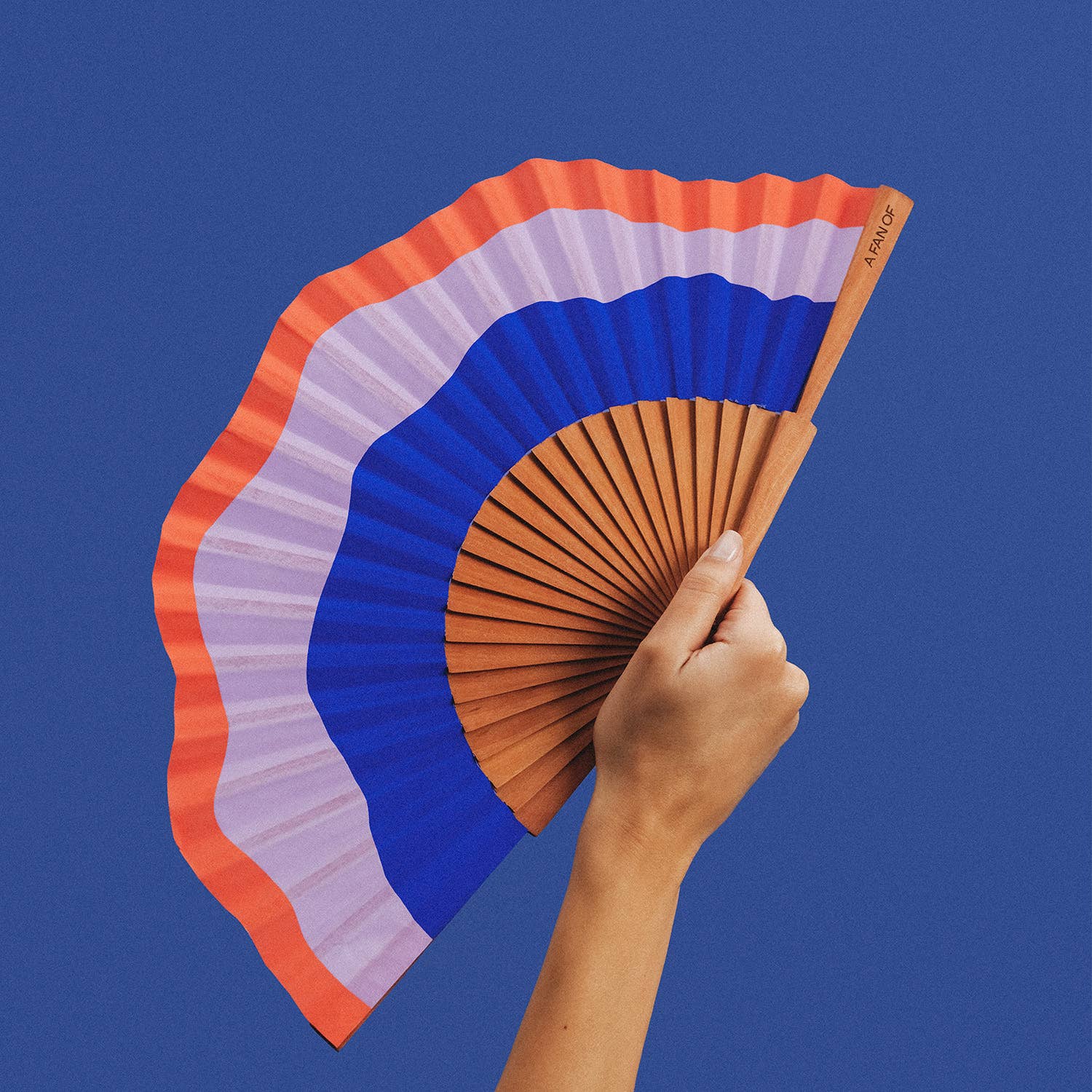A FAN OF Fluid Shapes MIDI fan in blue, lilac, and orange with 23 cm blades, showcasing a colorful, modern design.