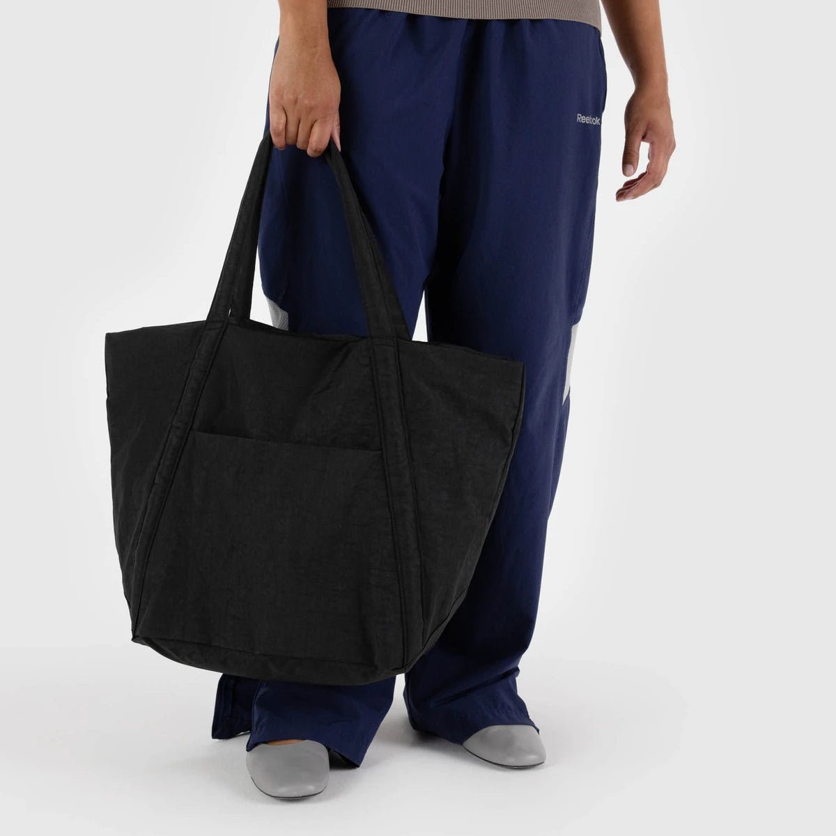 Person holding a black tote bag against a white background