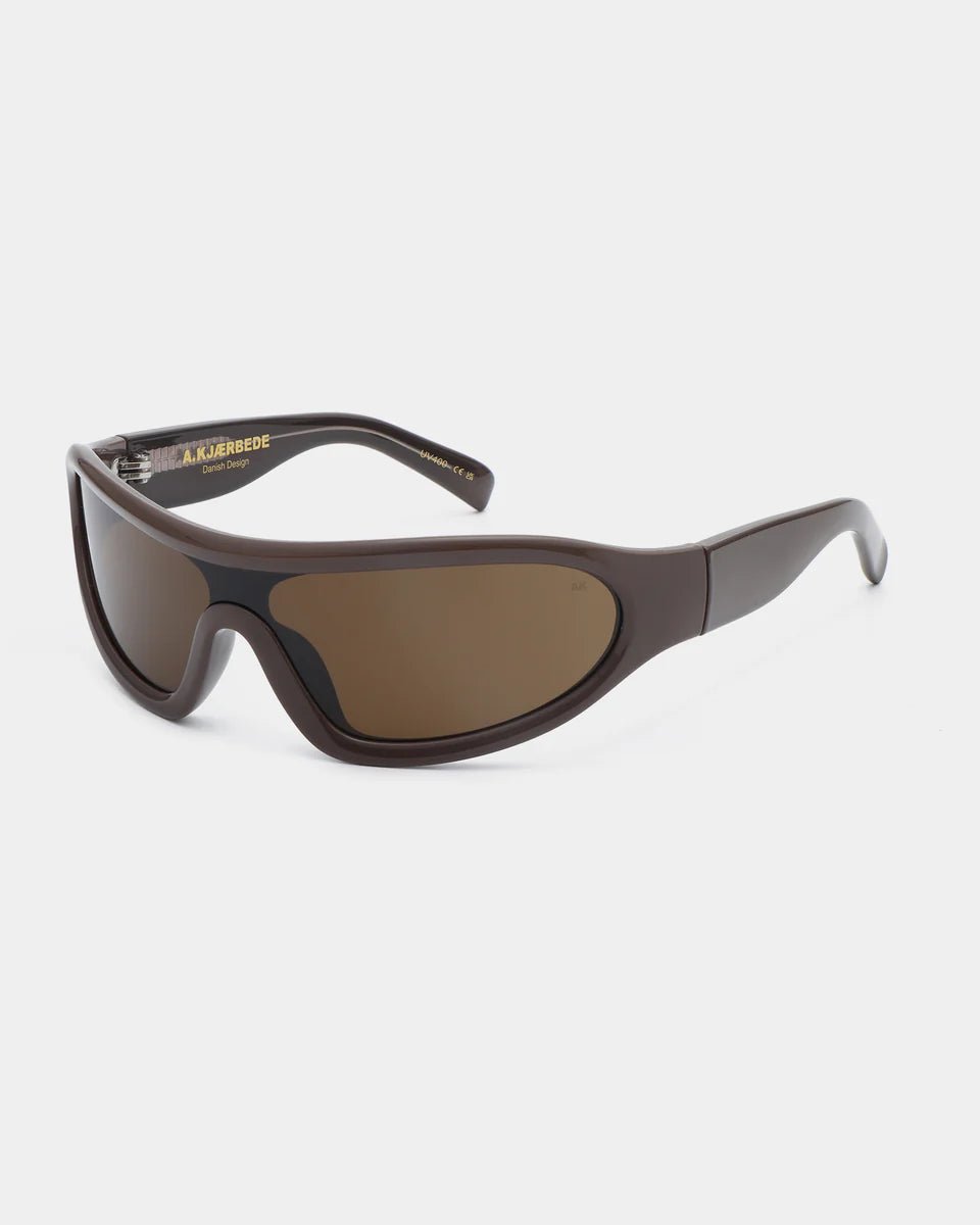 Chocolate brown Devon sunglasses by A. Kjaerbede with rounded frames and tinted lenses resting on a neutral surface.