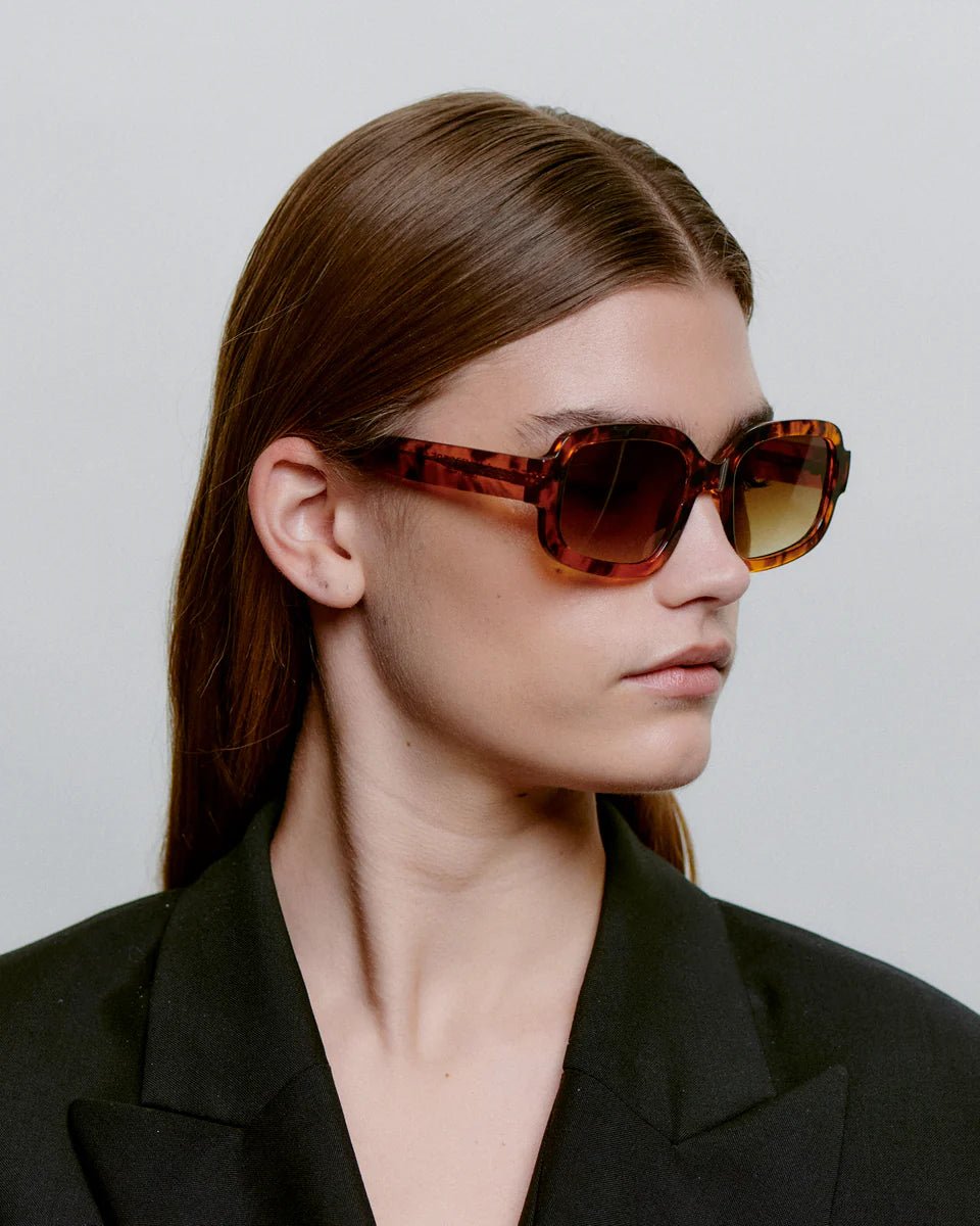 A. Kjaerbede Havana Pluto sunglasses with rounded frames and dark lenses, stylish eyewear on a white background.