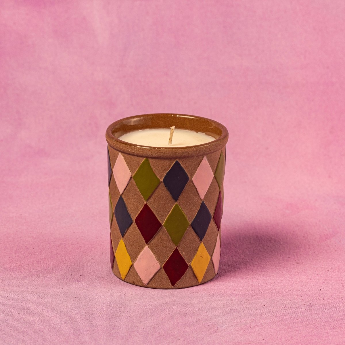 Candle in a diamond patterned container on a pink background