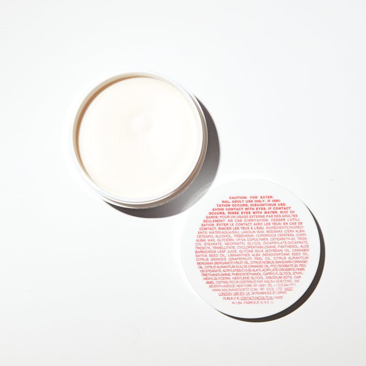 Malin+Goetz hair pomade in a jar, showing its creamy texture and sleek packaging for styling and grooming.
