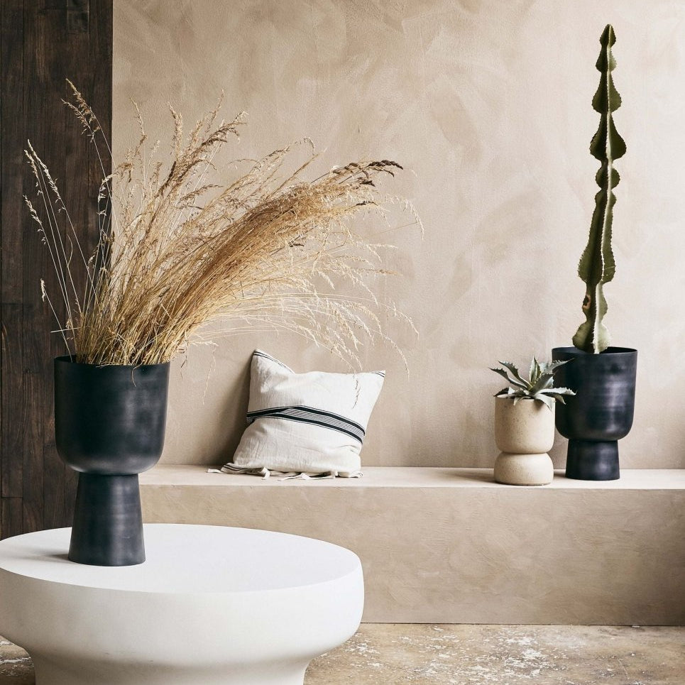 Decorative setting with plants and a pillow against a beige wall.