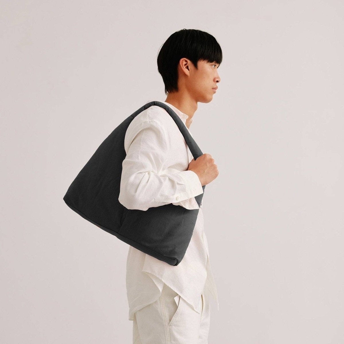 Person holding a dark gray tote bag against a plain background