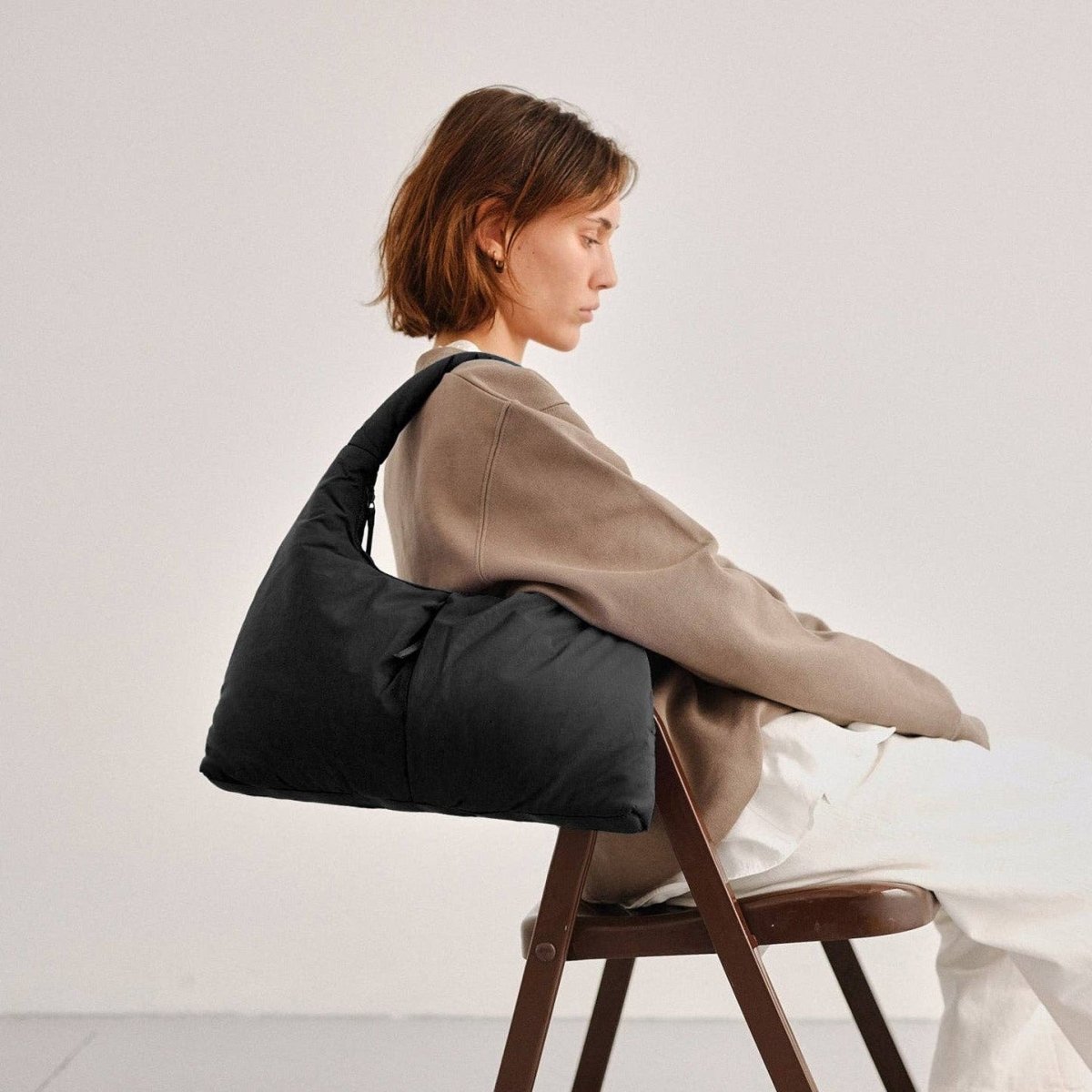 Woman sitting on a chair with a black bag over her shoulder against a plain background