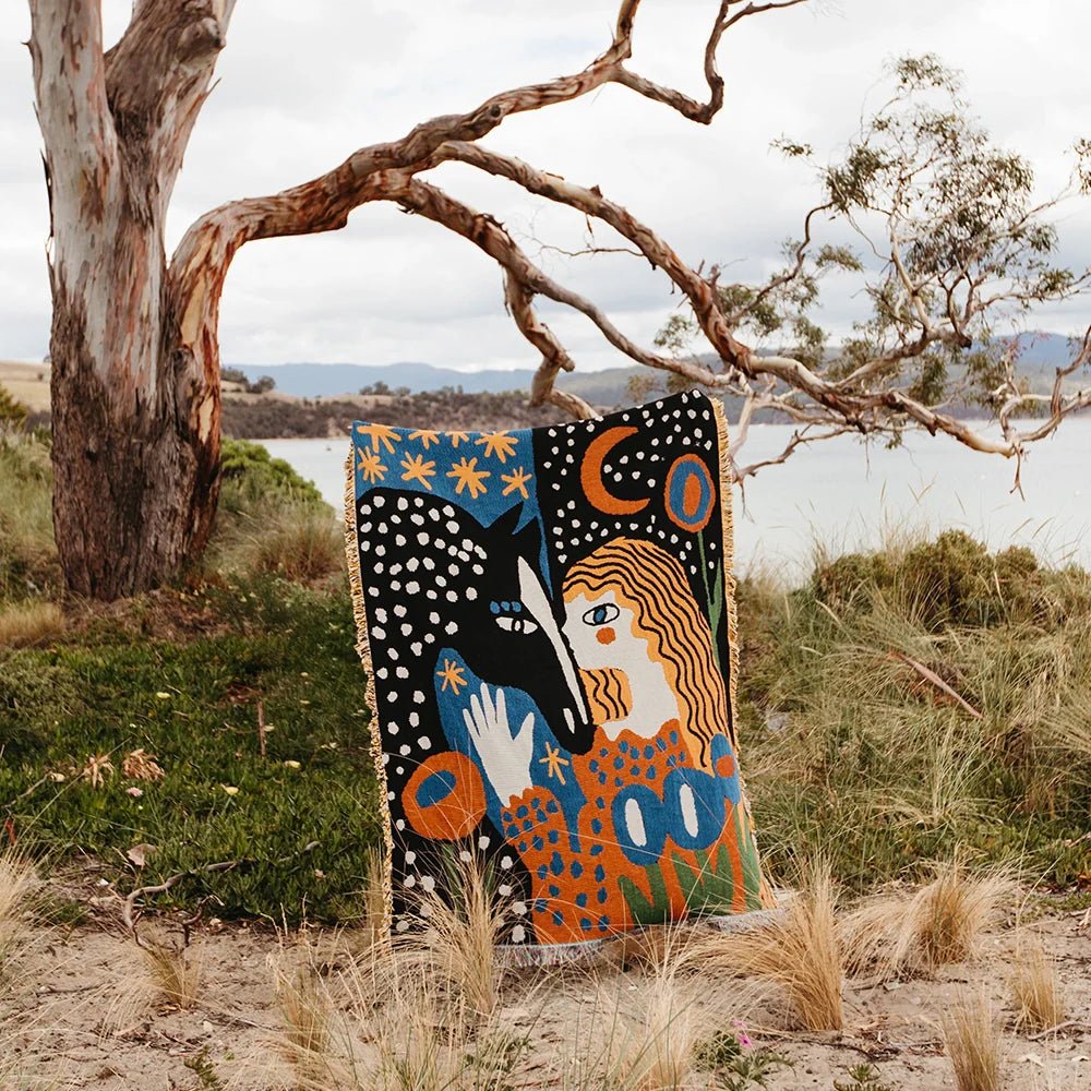 Colorful tapestry with abstract design in a natural setting with trees and water.