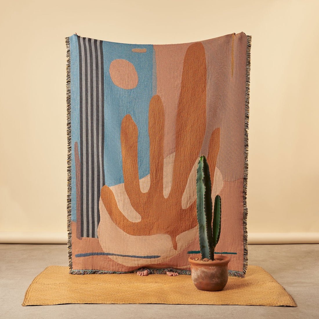 Earth tone woven blanket with an abstract desert landscape with a cactus in front of it and rug 