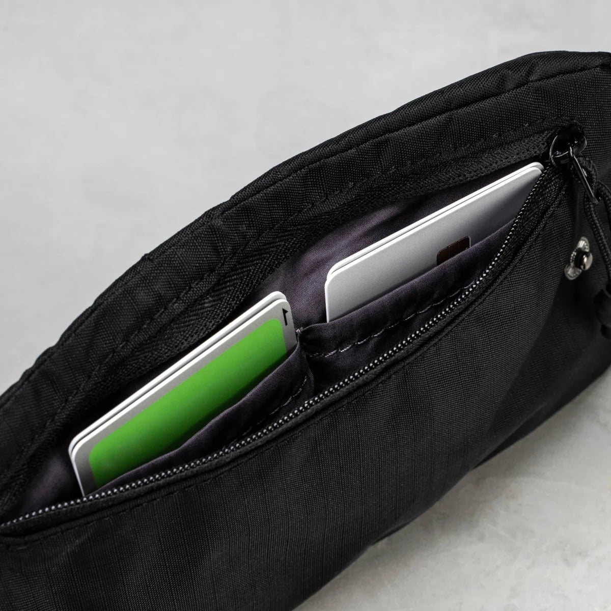 Black bag with compartments holding a green phone and a white device on a light gray background