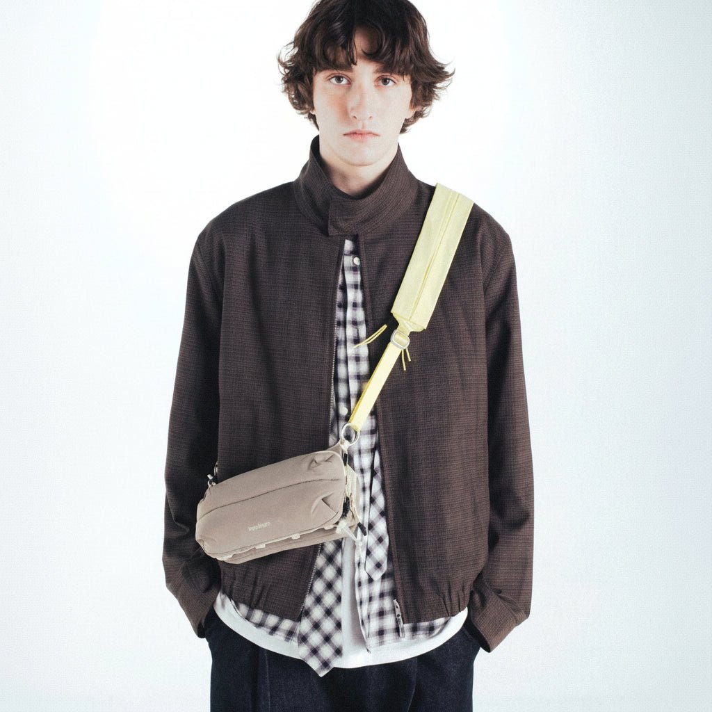 Person wearing a brown jacket with moss putty puffy bottle bag from topologie over one shoulder on a white background