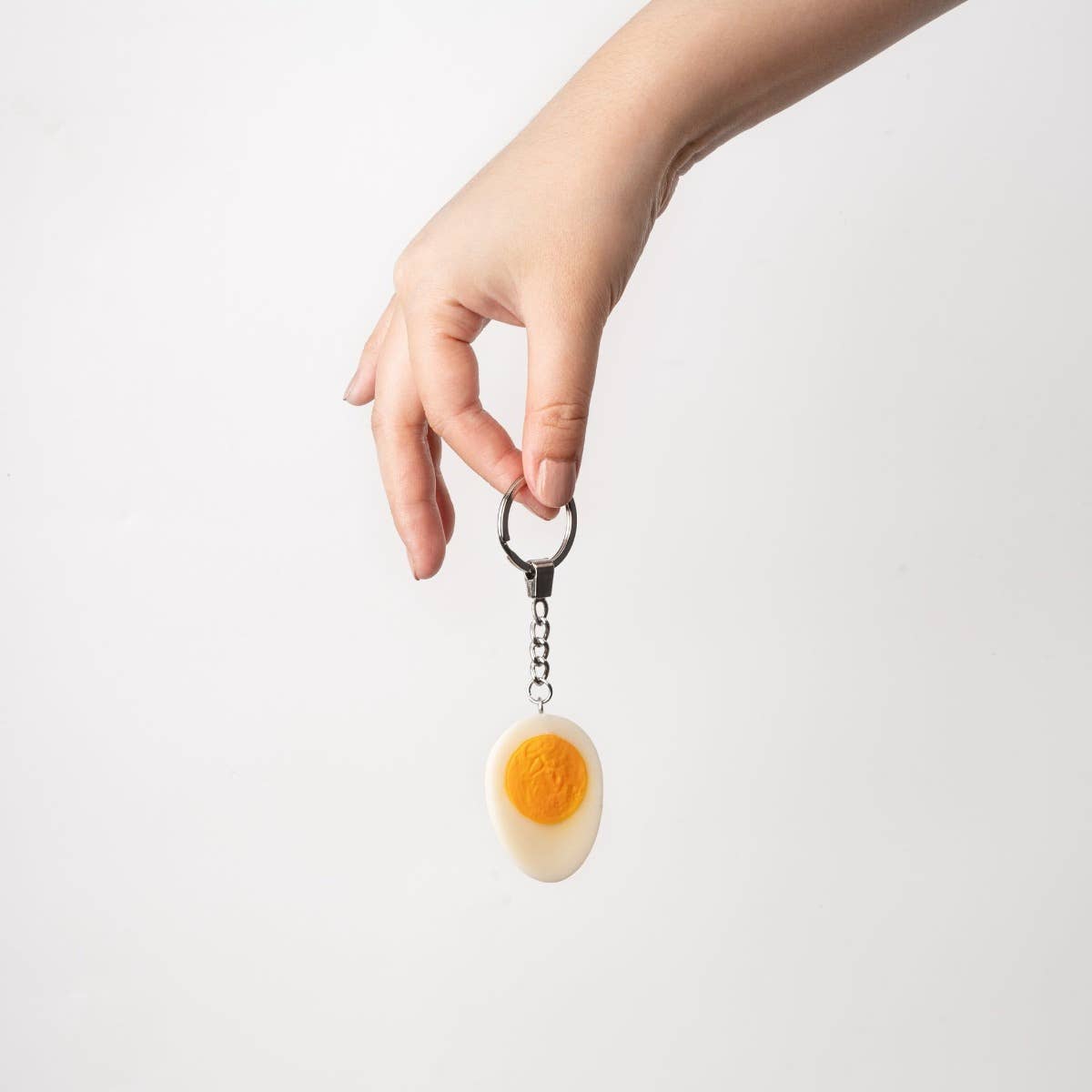 Hard-boiled egg keychain accessory by yumazing, featuring a realistic plastic egg design, attached to a silver keyring.